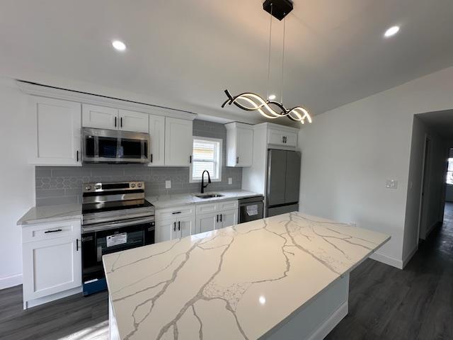 kitchen with a kitchen island, sink, white cabinets, hanging light fixtures, and stainless steel appliances