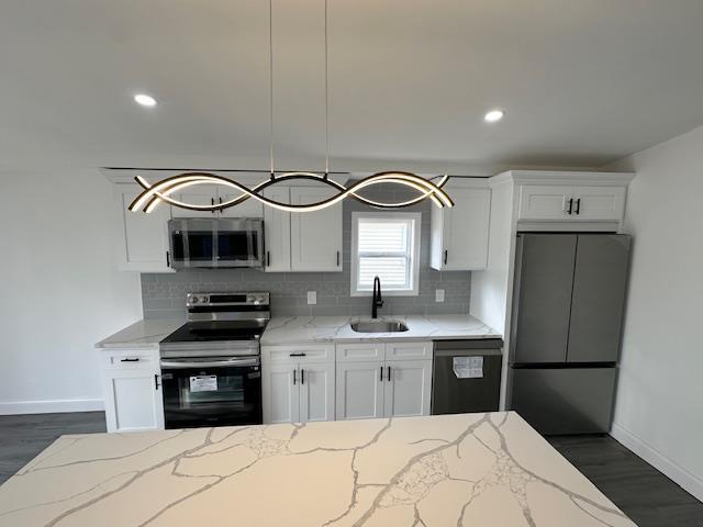 kitchen with sink, decorative light fixtures, appliances with stainless steel finishes, light stone countertops, and white cabinets