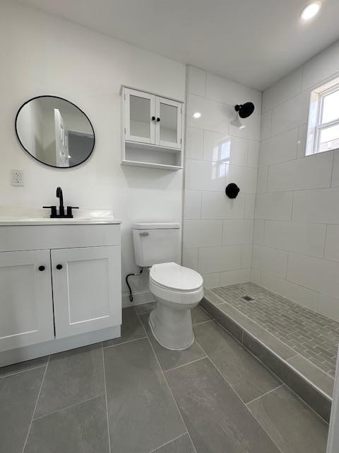 bathroom featuring vanity, toilet, and a tile shower