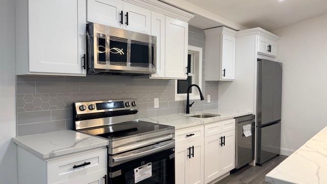 kitchen featuring sink, light stone counters, white cabinets, stainless steel appliances, and backsplash