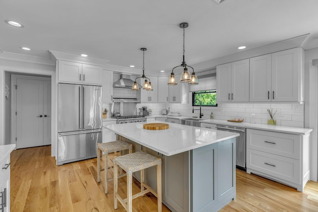 kitchen featuring pendant lighting, wall chimney range hood, stainless steel appliances, a kitchen island, and light wood-type flooring