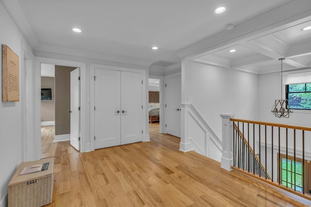 corridor with beamed ceiling, ornamental molding, coffered ceiling, and light hardwood / wood-style floors