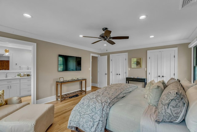 bedroom with ornamental molding, sink, two closets, and light wood-type flooring