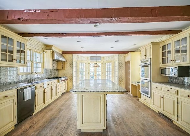 kitchen with wood-type flooring, a center island, appliances with stainless steel finishes, light stone countertops, and wall chimney range hood