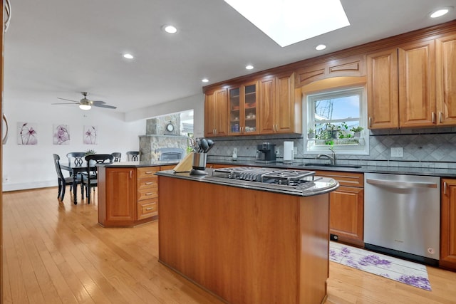 kitchen featuring dark countertops, a kitchen island, stainless steel appliances, light wood-type flooring, and a sink