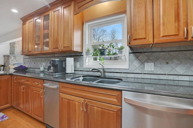 kitchen with a sink, dark stone countertops, brown cabinetry, and stainless steel dishwasher