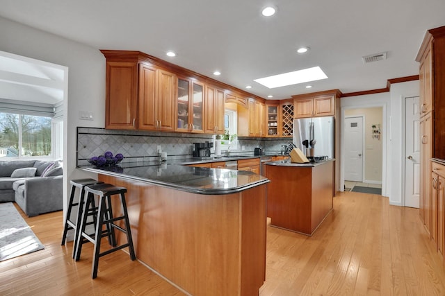 kitchen with a skylight, a center island, a peninsula, freestanding refrigerator, and light wood-type flooring