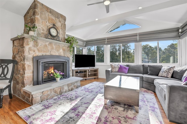 living area featuring lofted ceiling with beams, ceiling fan, wood finished floors, and a stone fireplace