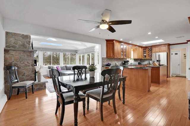 dining room featuring ornamental molding, a skylight, ceiling fan, and light wood finished floors