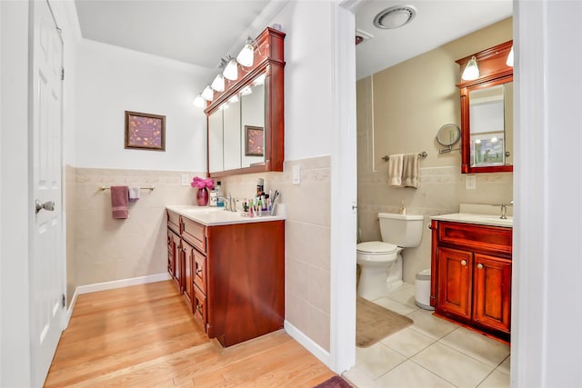 bathroom featuring toilet, a wainscoted wall, a sink, two vanities, and tile walls