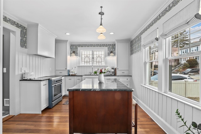 kitchen featuring high end range, decorative light fixtures, a center island, dark stone countertops, and dark hardwood / wood-style flooring