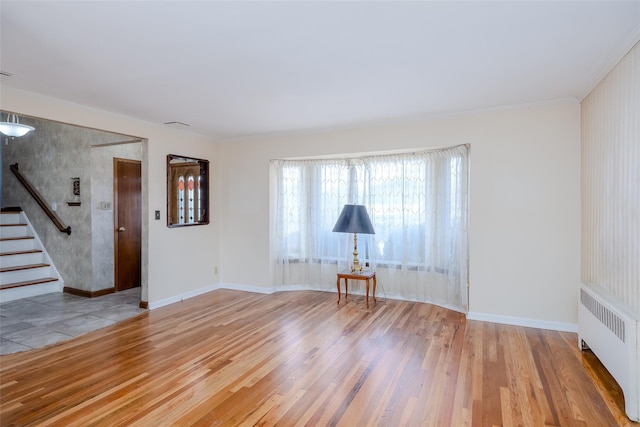 unfurnished room with crown molding, radiator, and light wood-type flooring