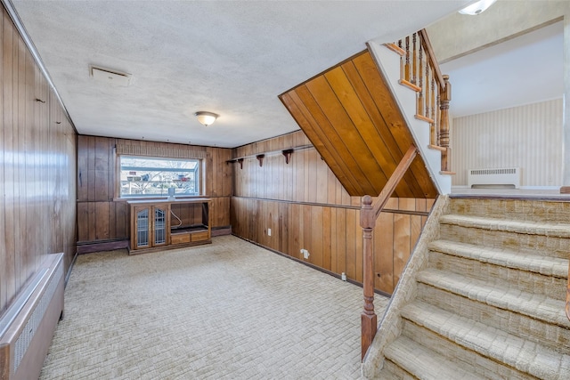 interior space featuring radiator, wooden walls, light colored carpet, and a textured ceiling