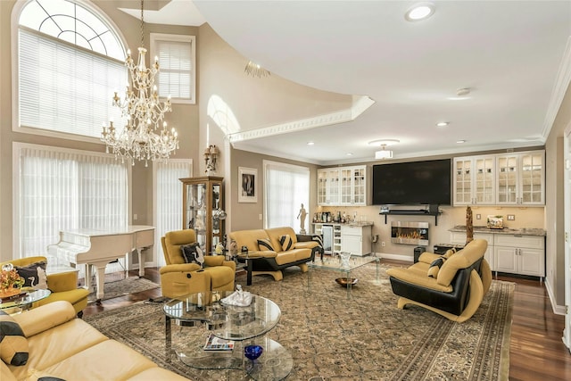 living area featuring dark wood finished floors, recessed lighting, an inviting chandelier, ornamental molding, and a glass covered fireplace