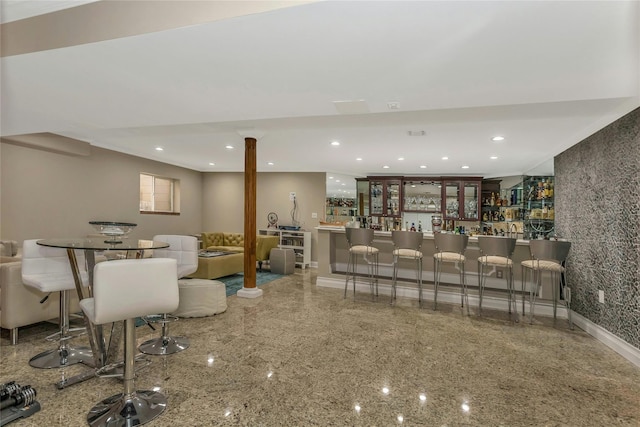 living room featuring granite finish floor, wet bar, baseboards, and recessed lighting