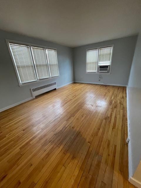 unfurnished room with cooling unit, radiator, and light hardwood / wood-style flooring