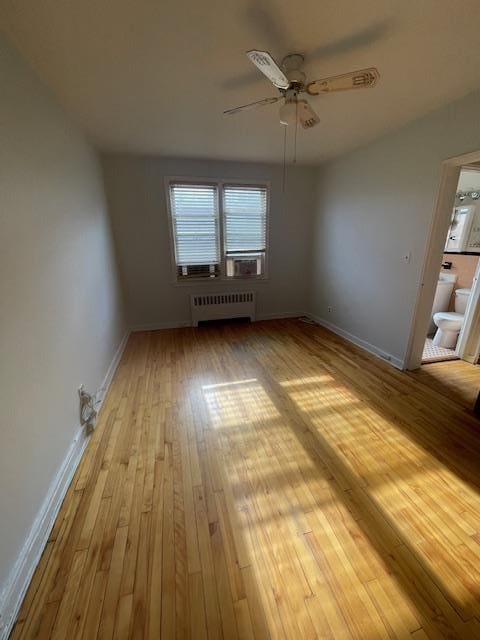 unfurnished room featuring ceiling fan, radiator heating unit, and light wood-type flooring