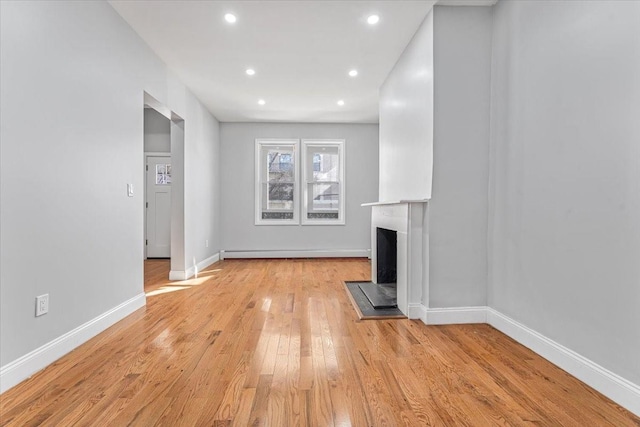 unfurnished living room with baseboard heating and light hardwood / wood-style floors