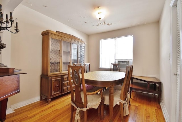 dining area with cooling unit, light hardwood / wood-style flooring, and an inviting chandelier