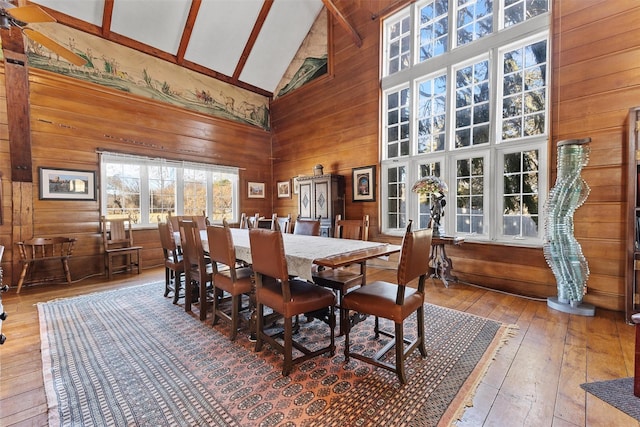 dining space with high vaulted ceiling, wood walls, and wood finished floors