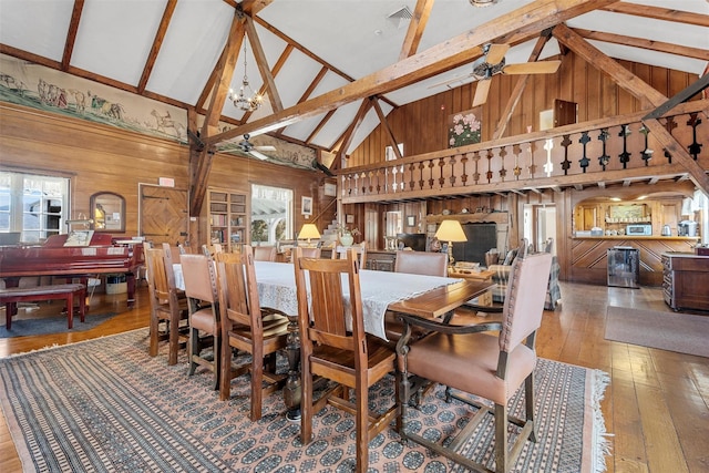 dining space with visible vents, wood finished floors, vaulted ceiling with beams, wood walls, and ceiling fan with notable chandelier