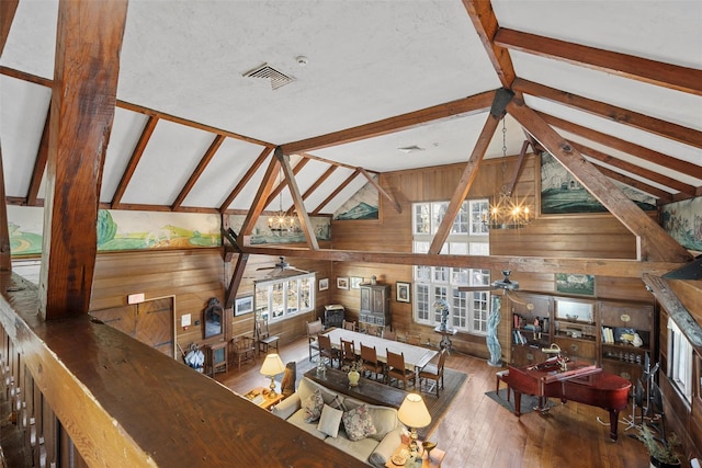 living area with vaulted ceiling with beams, visible vents, wood walls, wood finished floors, and ceiling fan with notable chandelier