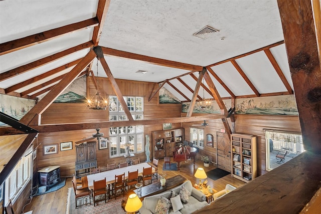 unfurnished living room featuring visible vents, vaulted ceiling with beams, wood walls, and ceiling fan with notable chandelier