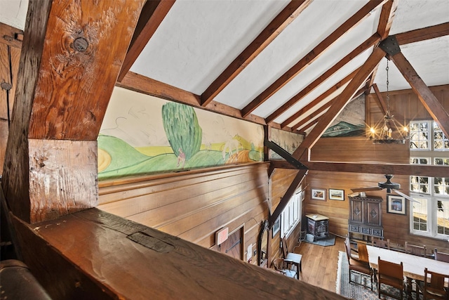 interior space with vaulted ceiling with beams, a notable chandelier, wood walls, wood finished floors, and a wood stove