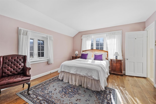 bedroom with light wood-type flooring, vaulted ceiling, and baseboards