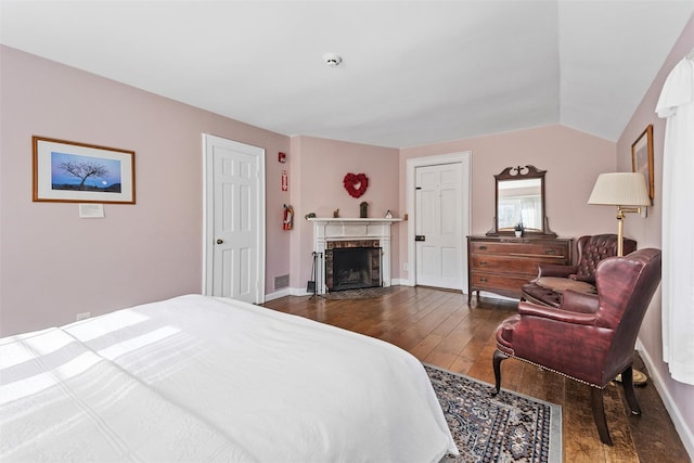 bedroom with lofted ceiling, dark wood-style flooring, a fireplace with flush hearth, visible vents, and baseboards