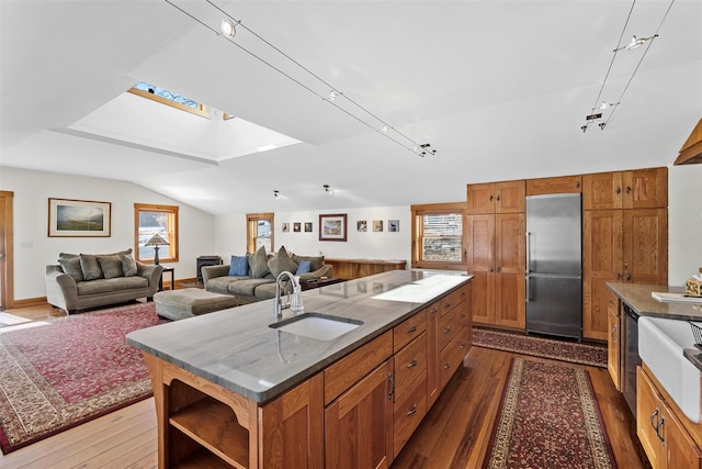 kitchen featuring vaulted ceiling with skylight, brown cabinetry, an island with sink, appliances with stainless steel finishes, and a sink