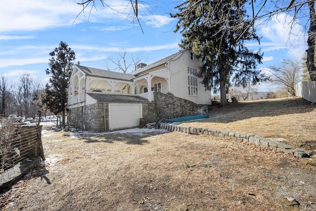 view of property exterior featuring a garage, stone siding, dirt driveway, and fence