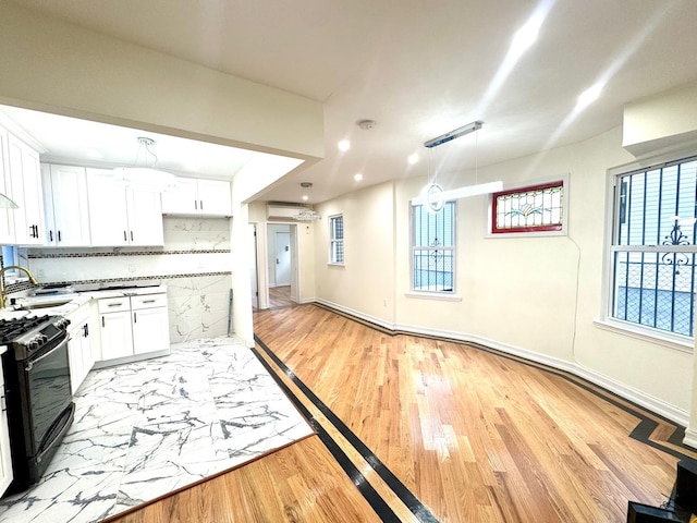 kitchen featuring sink, white cabinetry, black gas range oven, a wall unit AC, and decorative backsplash