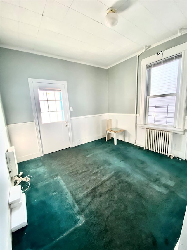 carpeted spare room featuring crown molding and radiator heating unit