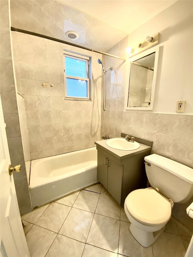 full bathroom with toilet, tiled shower / bath, tile walls, vanity, and tile patterned flooring