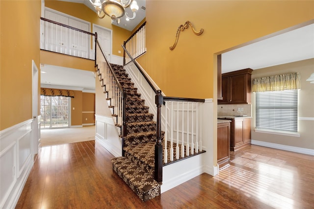 stairs featuring a towering ceiling, hardwood / wood-style floors, and a notable chandelier