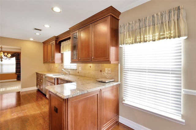 kitchen with sink, dark wood-type flooring, light stone counters, tasteful backsplash, and a chandelier