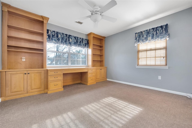 unfurnished office with light carpet, built in desk, and ceiling fan