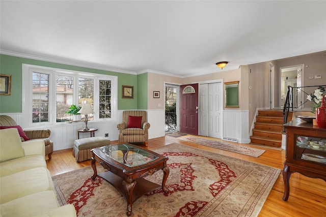 living area with light wood finished floors, crown molding, stairway, and a wainscoted wall