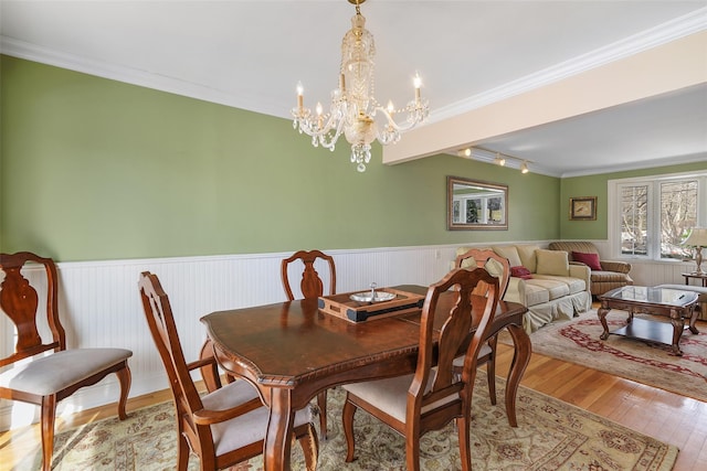 dining space with light wood finished floors, ornamental molding, and wainscoting