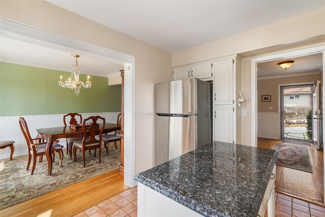 kitchen featuring a wainscoted wall, white cabinetry, freestanding refrigerator, dark stone counters, and pendant lighting