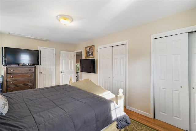 bedroom with wood finished floors, two closets, and baseboards