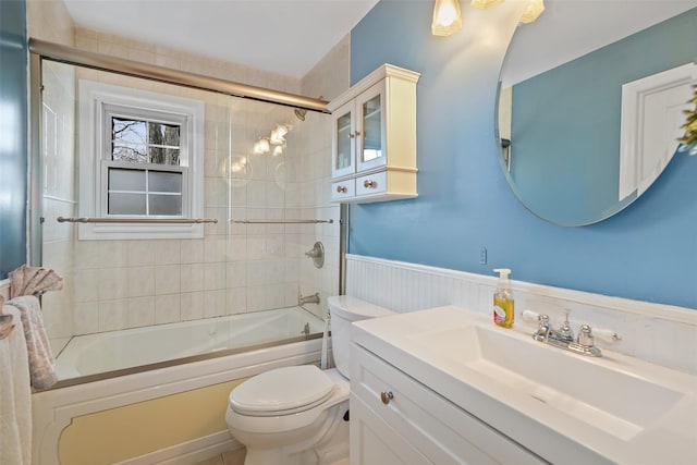 full bath with combined bath / shower with glass door, wainscoting, vanity, and toilet