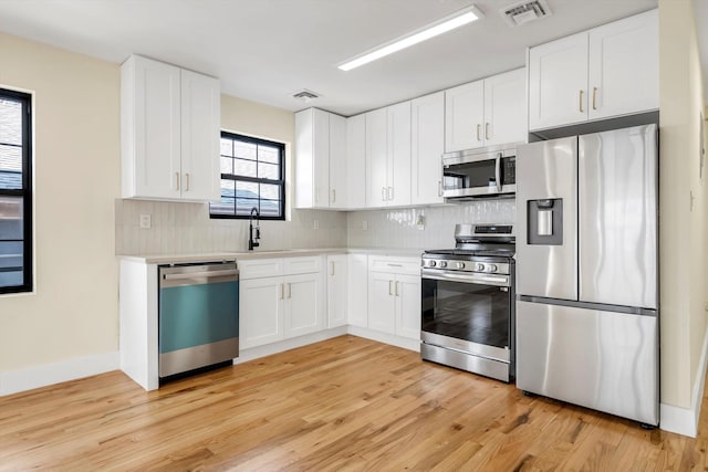 kitchen with backsplash, light wood-type flooring, white cabinets, and appliances with stainless steel finishes