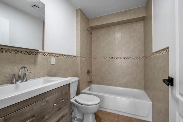 full bathroom with tile walls, vanity, tiled shower / bath, tile patterned floors, and toilet