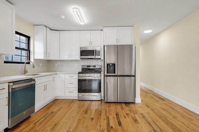 kitchen with sink, white cabinetry, stainless steel appliances, light hardwood / wood-style floors, and backsplash