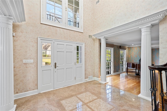 foyer entrance with a towering ceiling, ornamental molding, and ornate columns