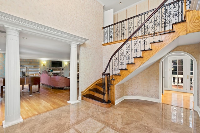 stairs with a towering ceiling, ornamental molding, wood-type flooring, and ornate columns