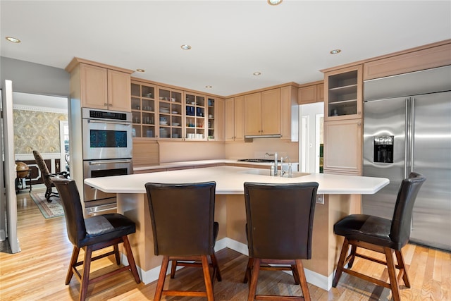 kitchen with stainless steel appliances, a large island, light brown cabinetry, and light hardwood / wood-style flooring