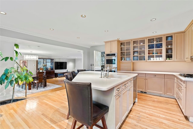 kitchen featuring a breakfast bar area, light brown cabinets, a kitchen island with sink, stainless steel appliances, and light hardwood / wood-style floors